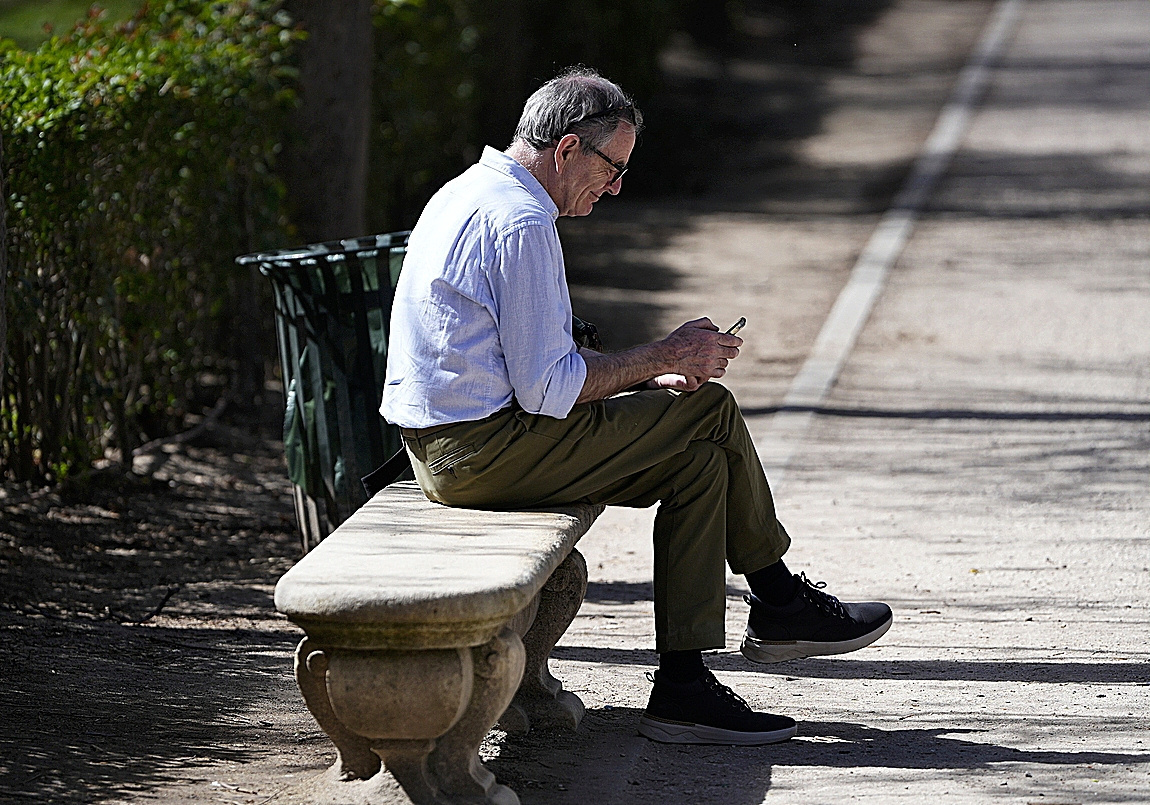 Un hombre utiliza su telfono en un parque en Madrid.