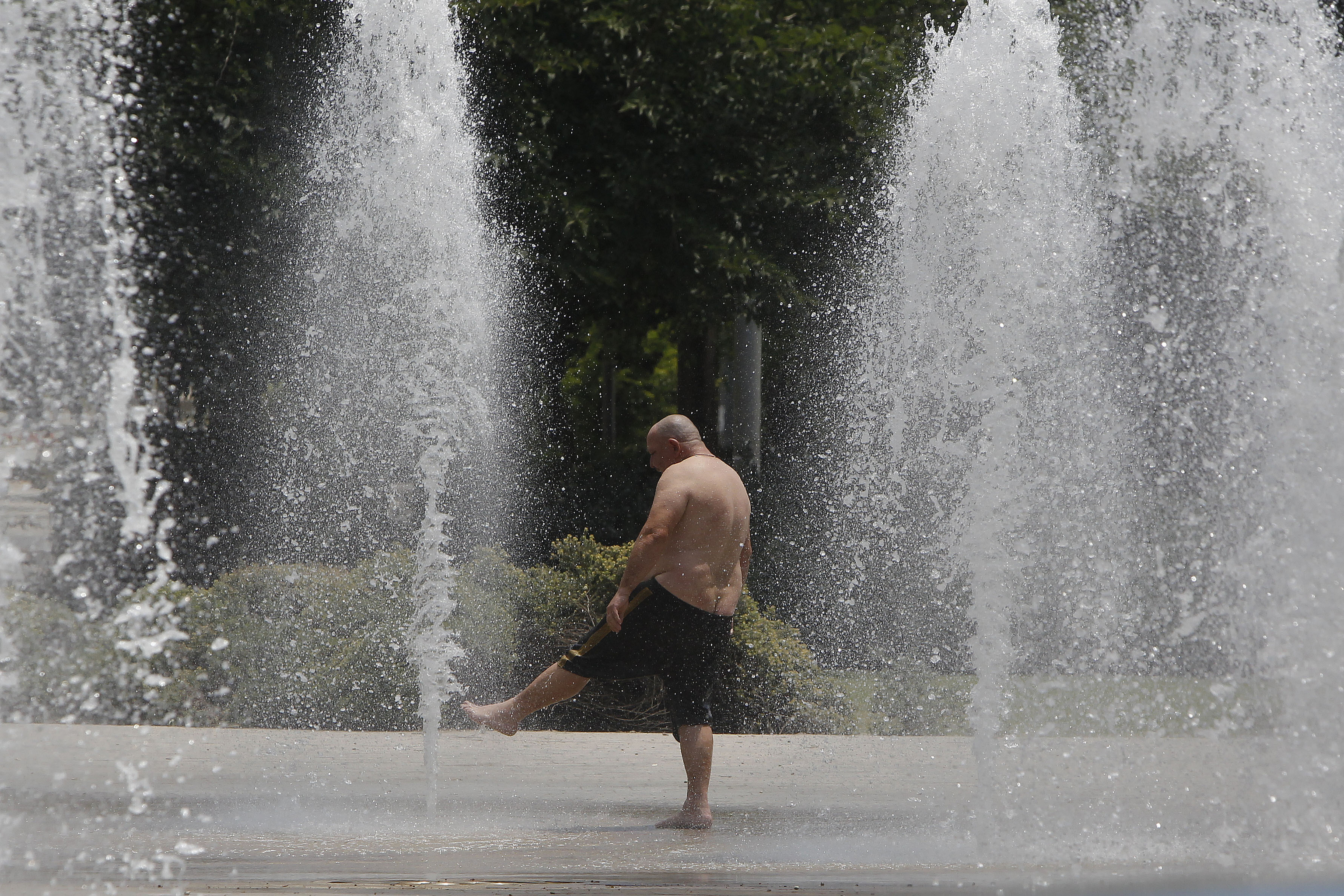 Un hombre se refresca en una fuente ante el calor extremo en Alicante.