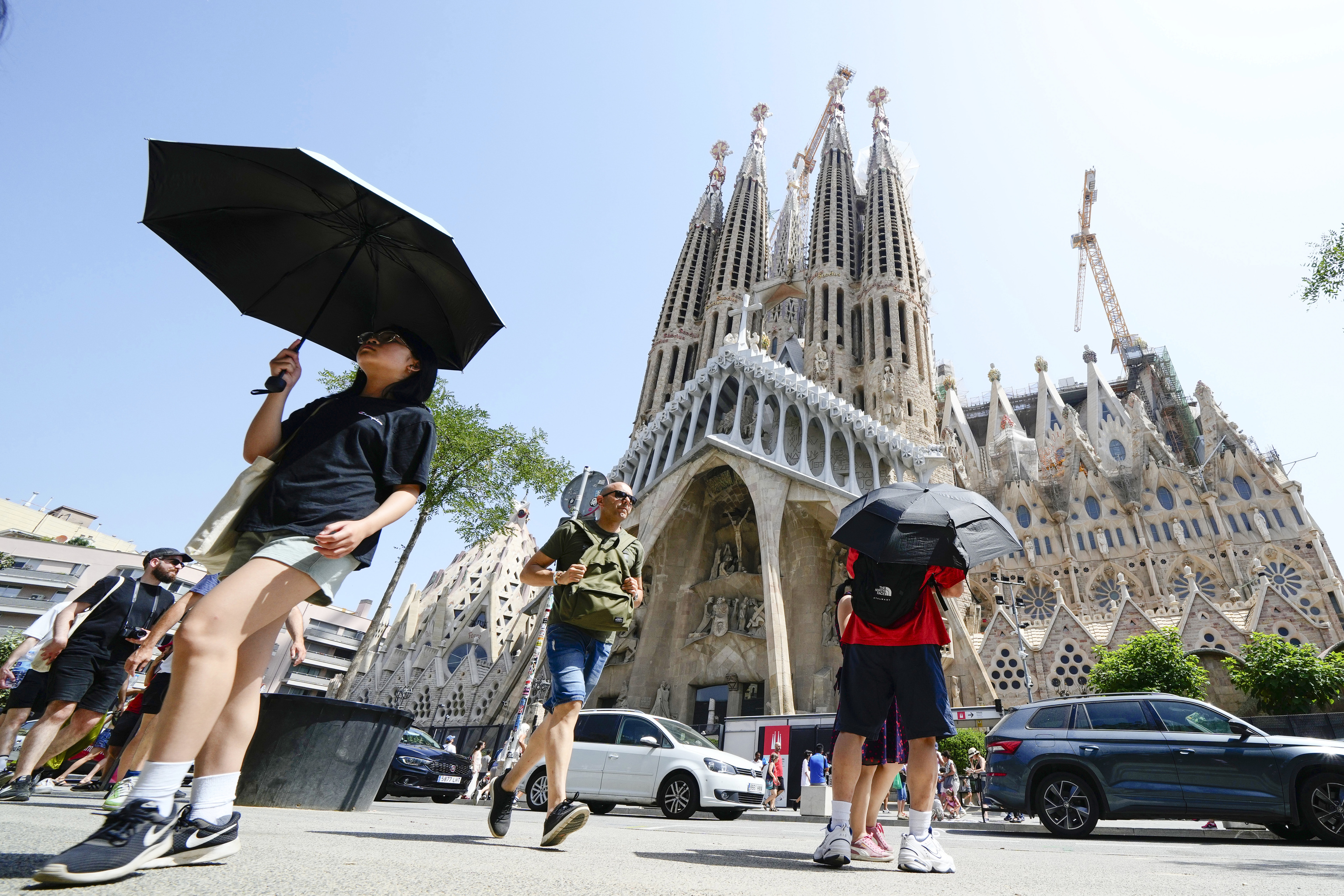 Varios turistas se protegen del sol bajo un paraguas ante la Sagrada Familia de Barcelona en plena ola de calor.