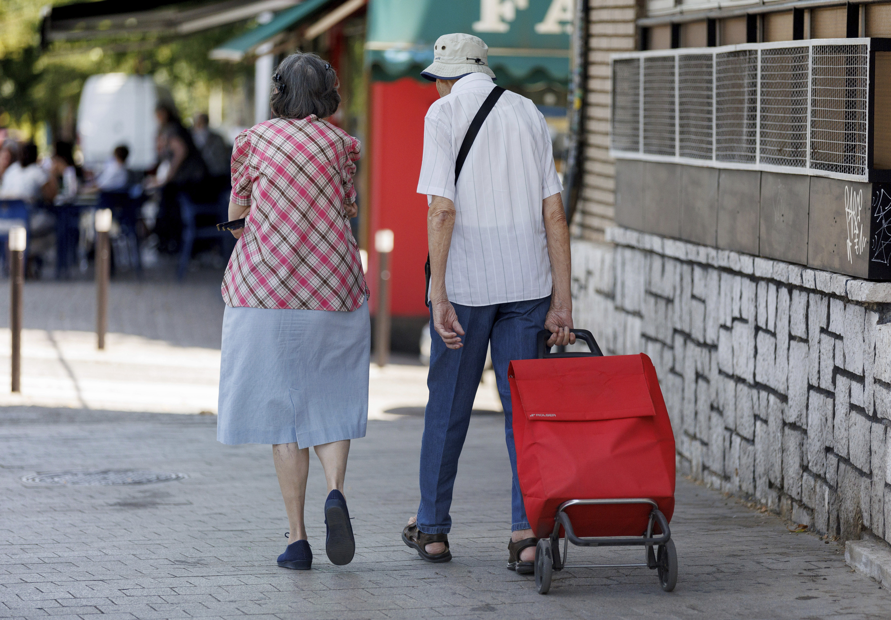 Una pareja de pensionistas camina con un carro de la compra
