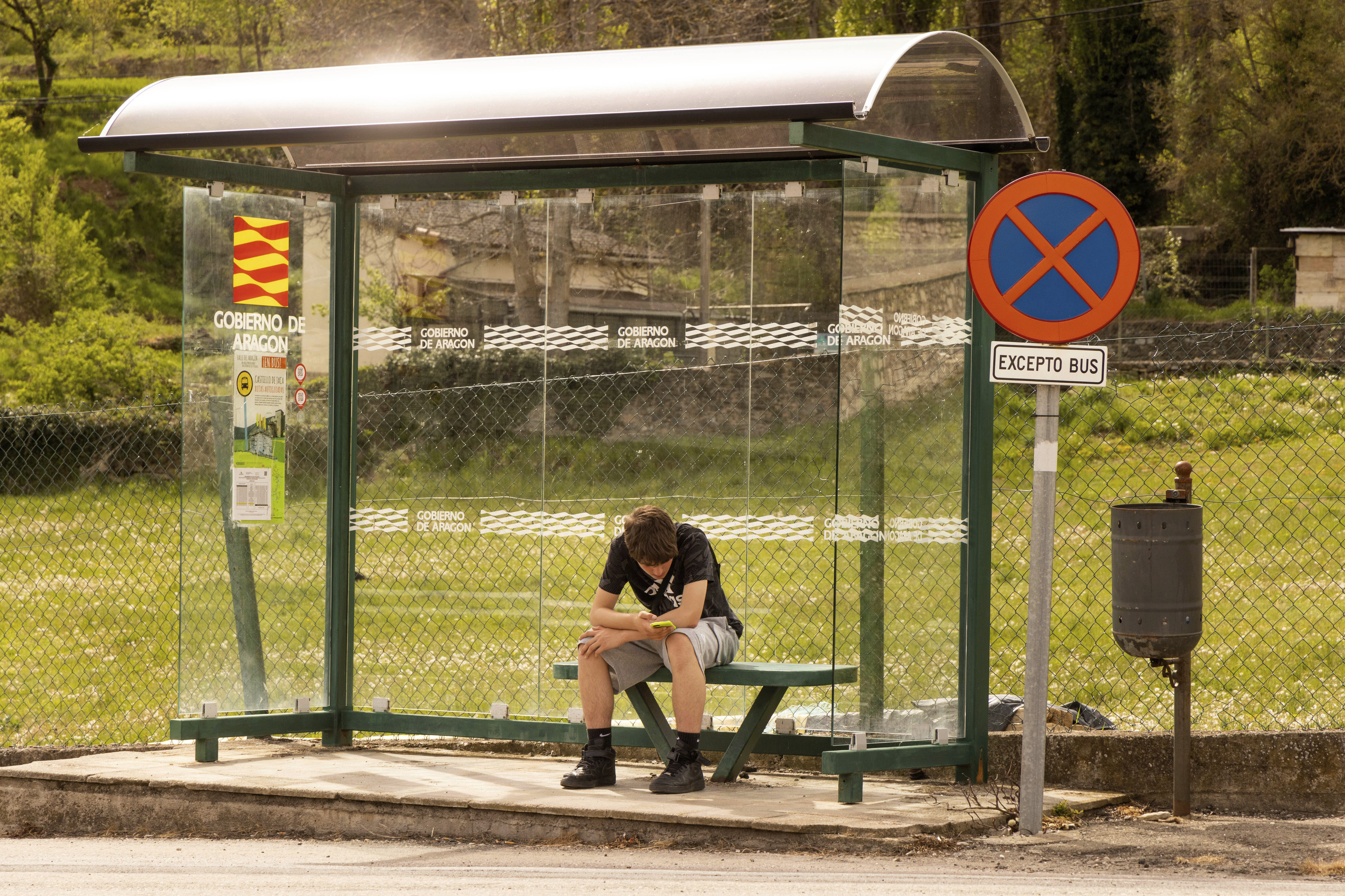 Un joven espera en la parada del autobús mientras mira el móvil