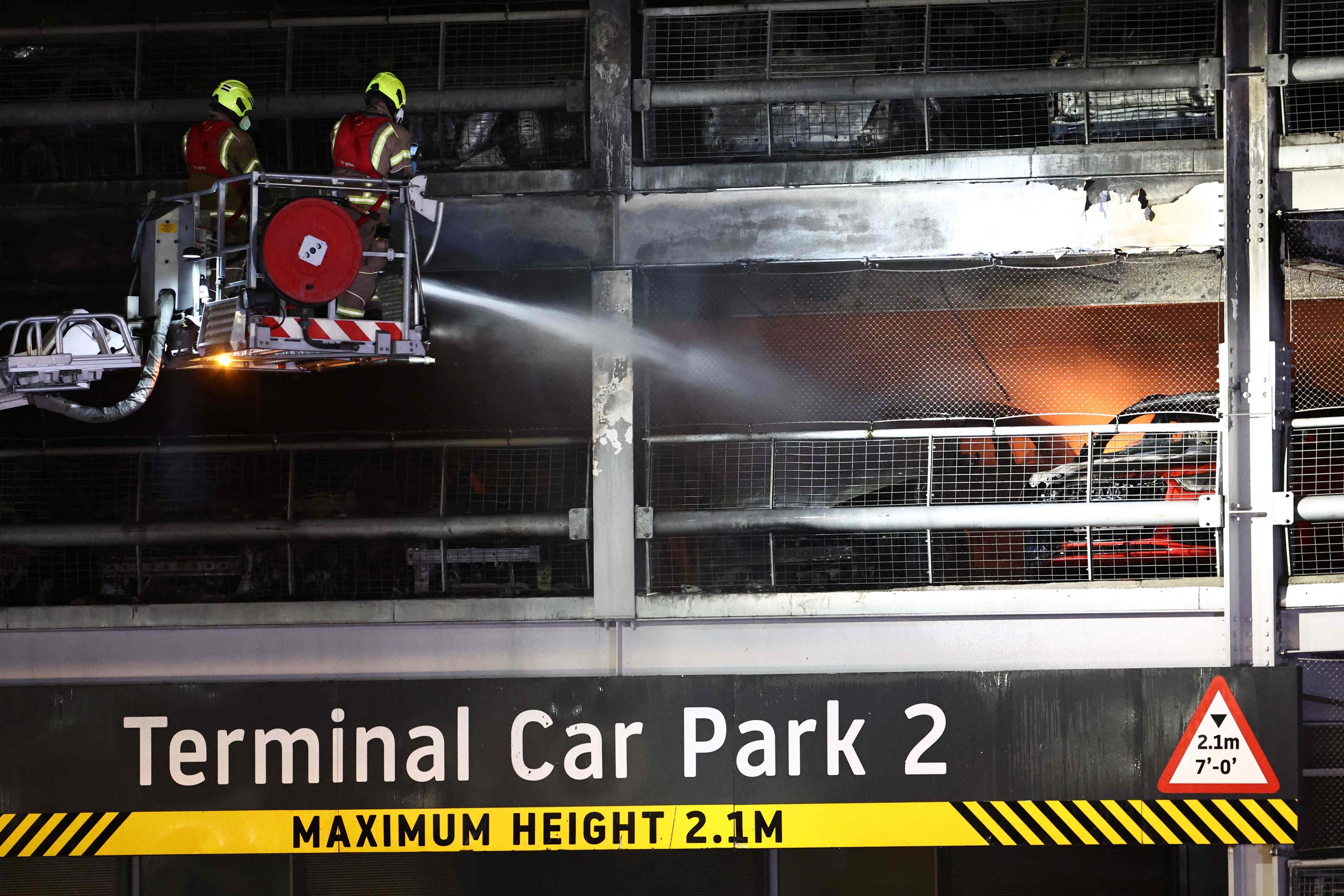 Los bomberos tratan de apagar el fuego originado en un aparcamiento.