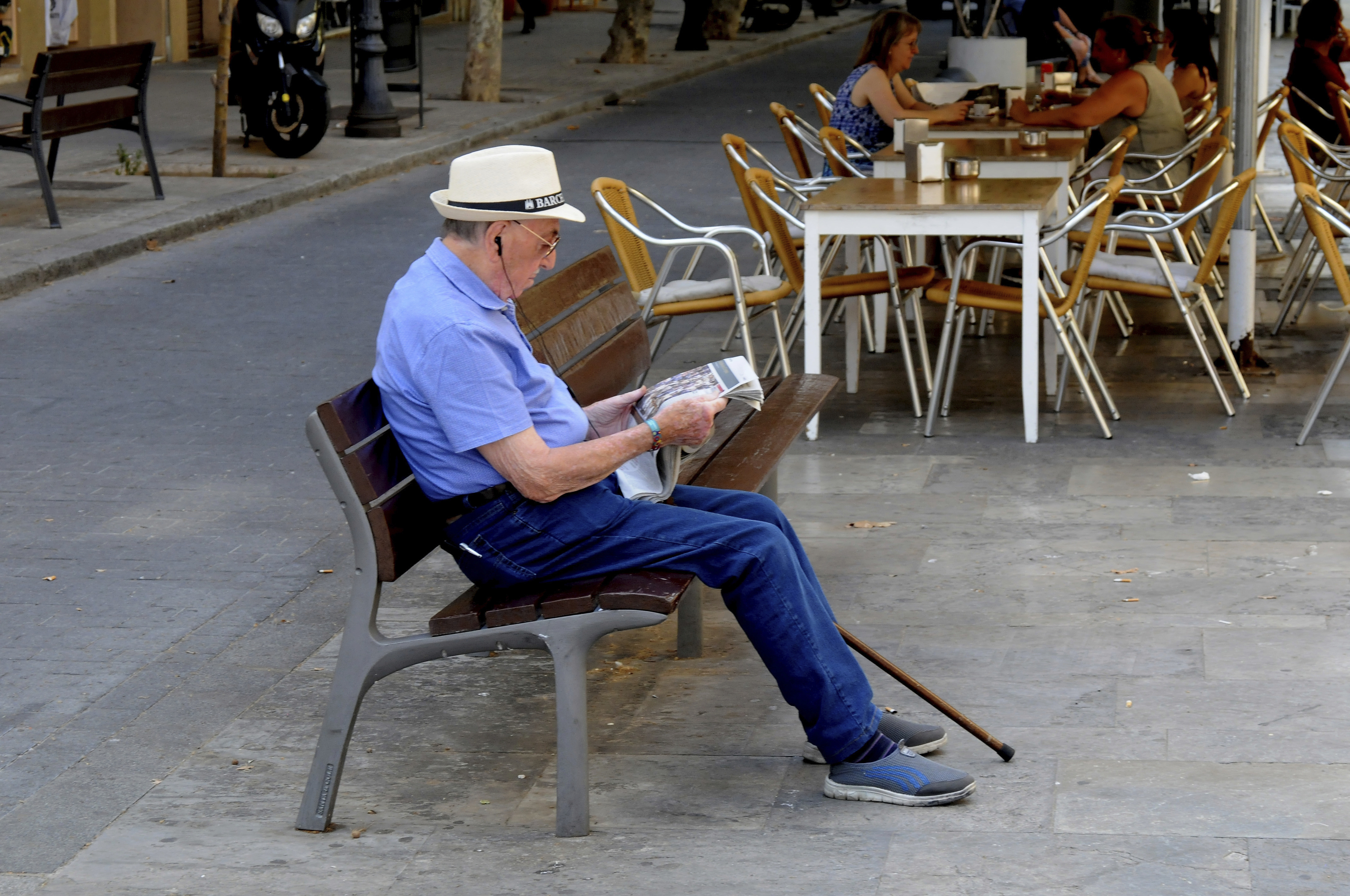Un jubilado sentando en un banco leyendo el peridico.
