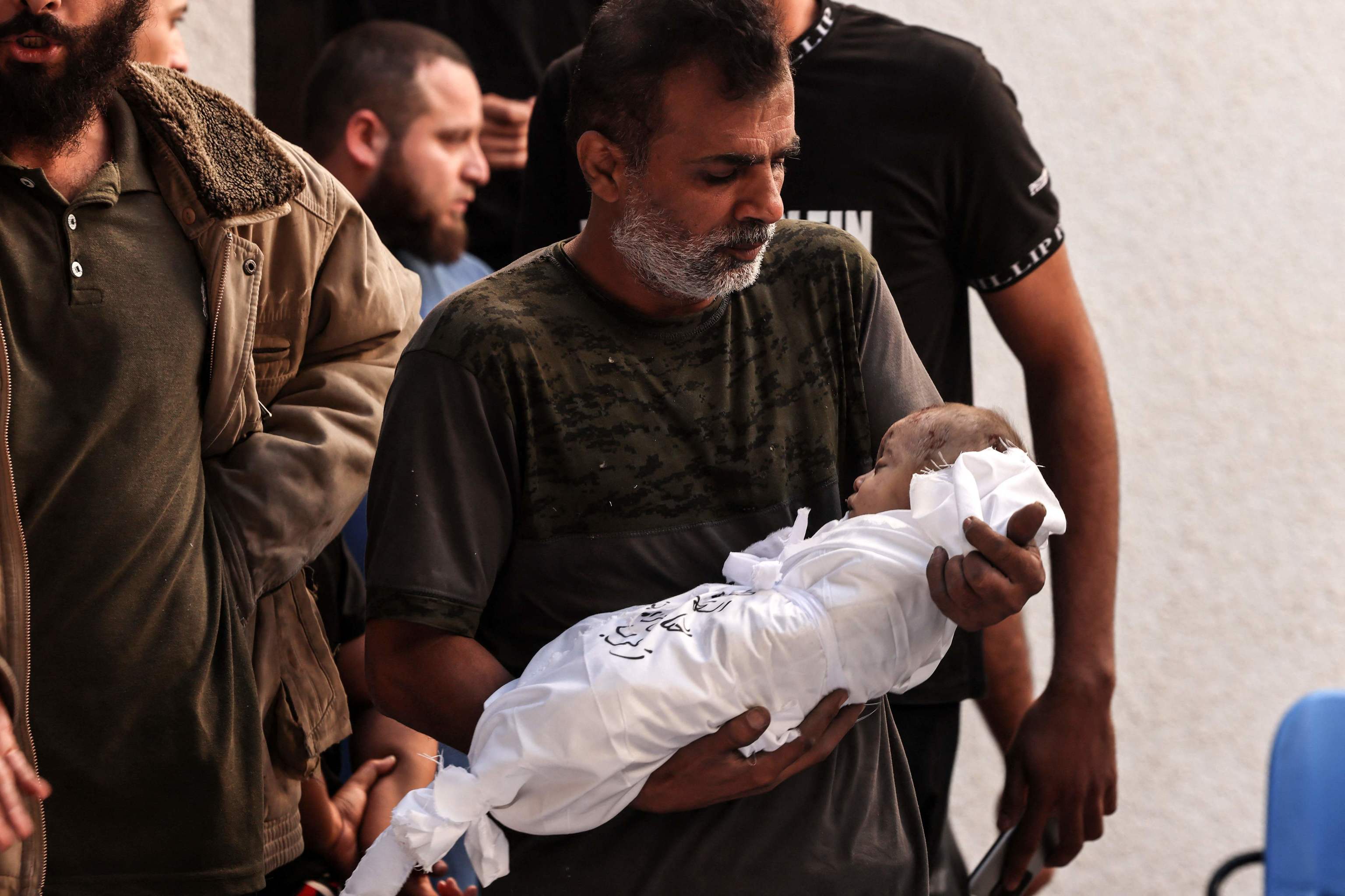Un hombre lleva en brazos a un bebé muerto.