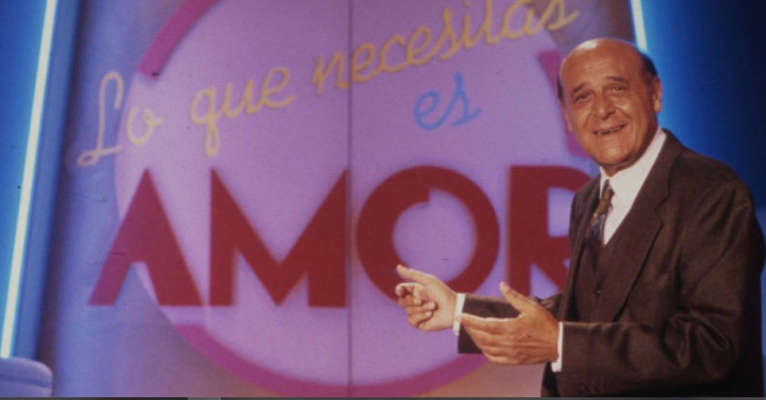 El presentador Jesús Puente delante de la carátula del programa 'Lo que necesitas es amor'.