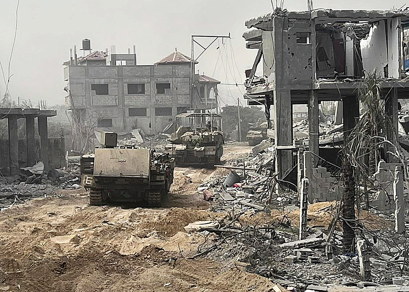 Vehculos blindados  avanzan entre edificios destruidos durante una operacin terrestre.