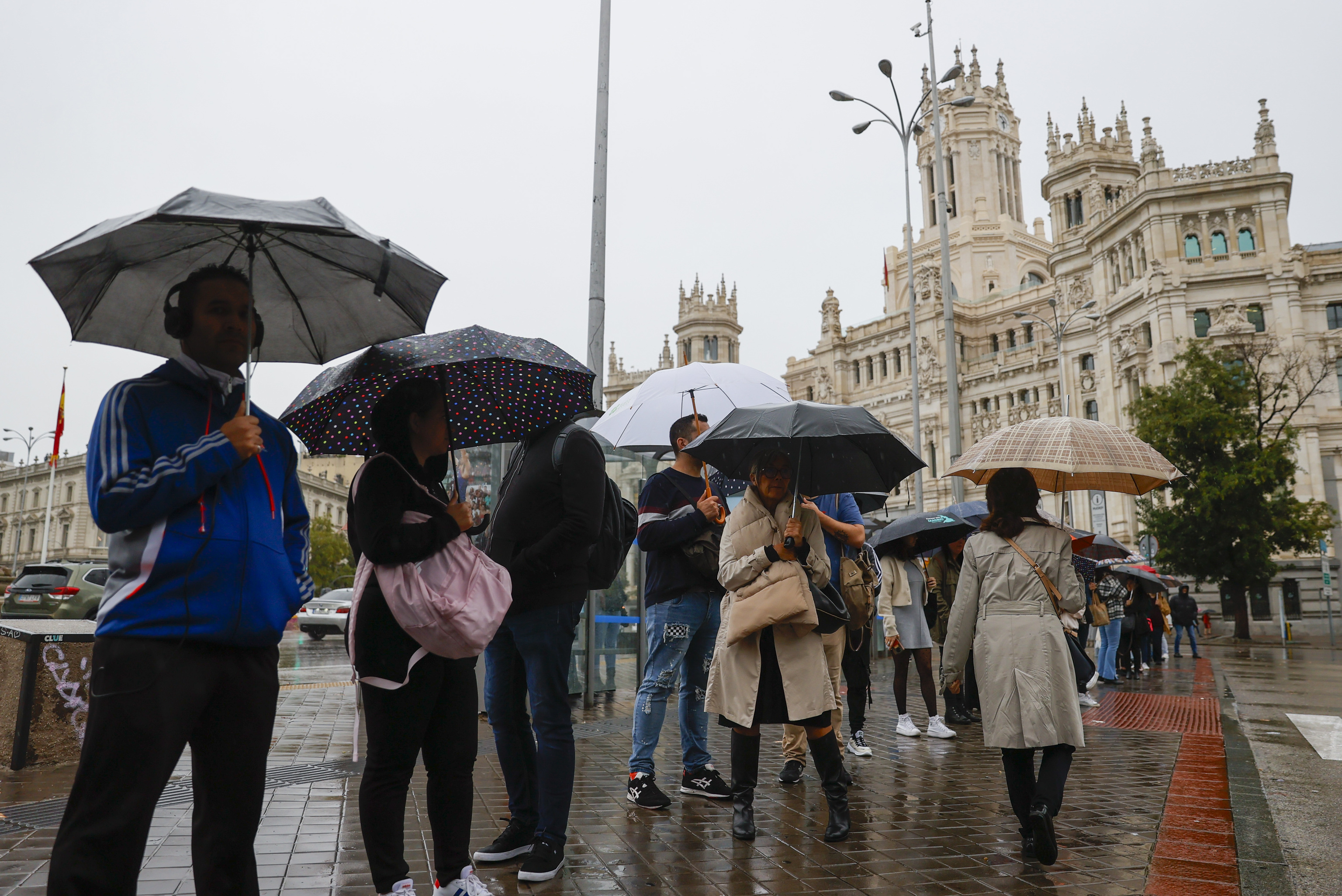 Varias personas se protegen de la lluvia con paraguas frente al Palacio de Cibeles de Madrid.