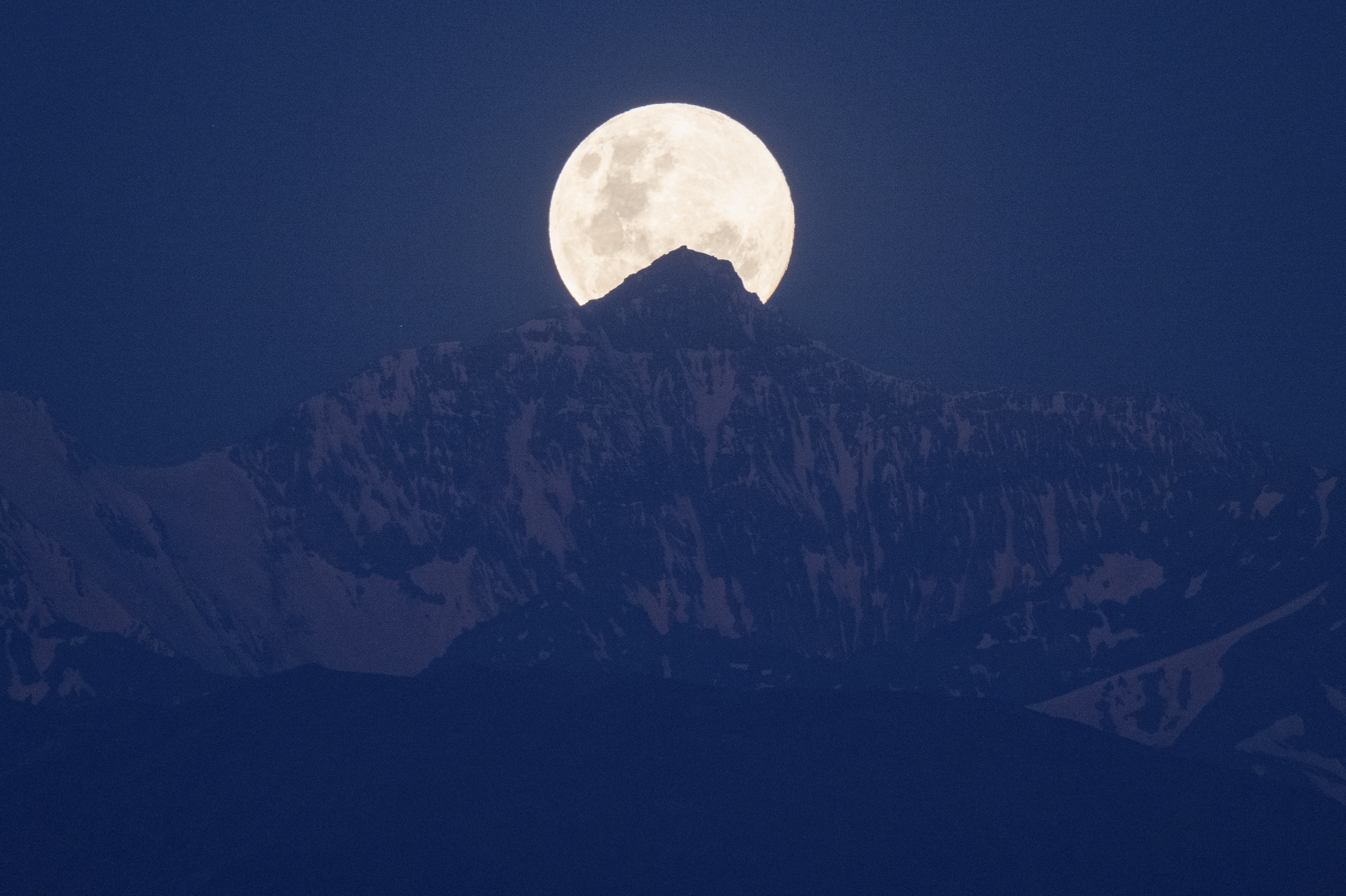 La luna llena, tras unas montañas.