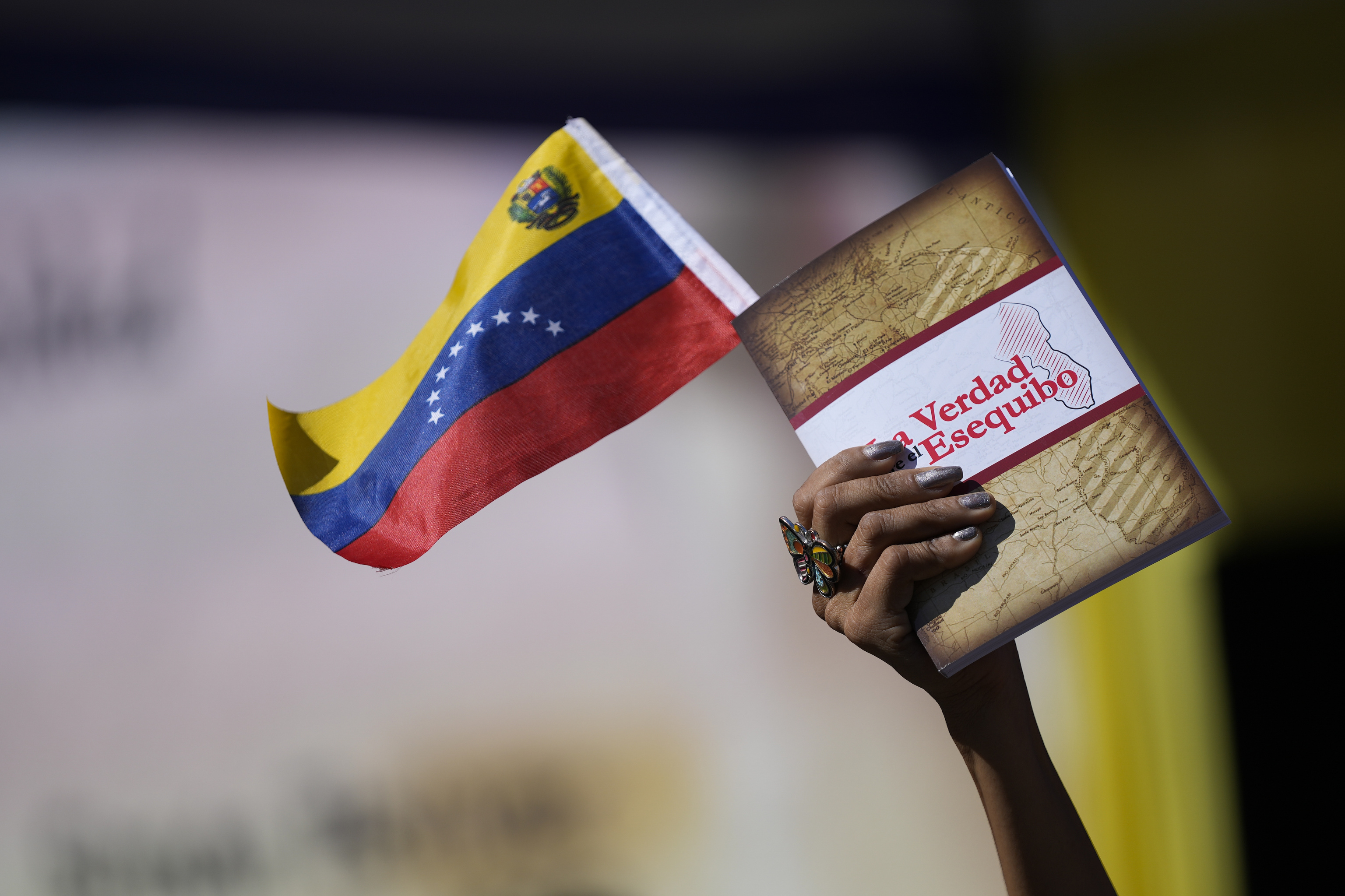 Una mujer sostiene una bandera venezolana y un libro sobre la disputa del territorio de Esequibo en Caracas