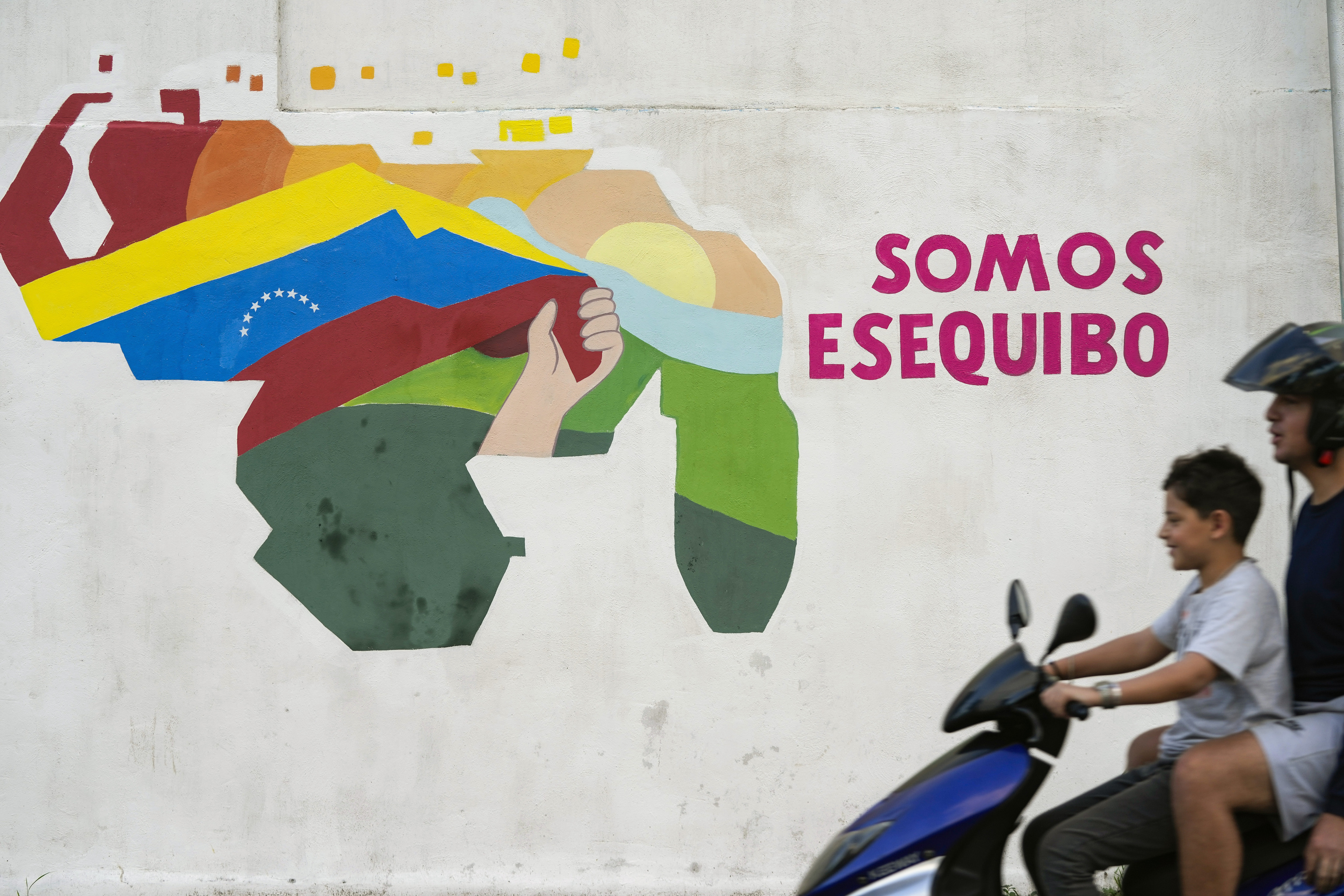 Un nio conduce una motocicleta por delante de un mural con el mapa de Venezuela, que incluye el territorio de Esequibo, en el vecindario 23 de Enero de Caracas, Venezuela, el 11 de diciembre de 2023. (AP Foto/Matas Delacroix)