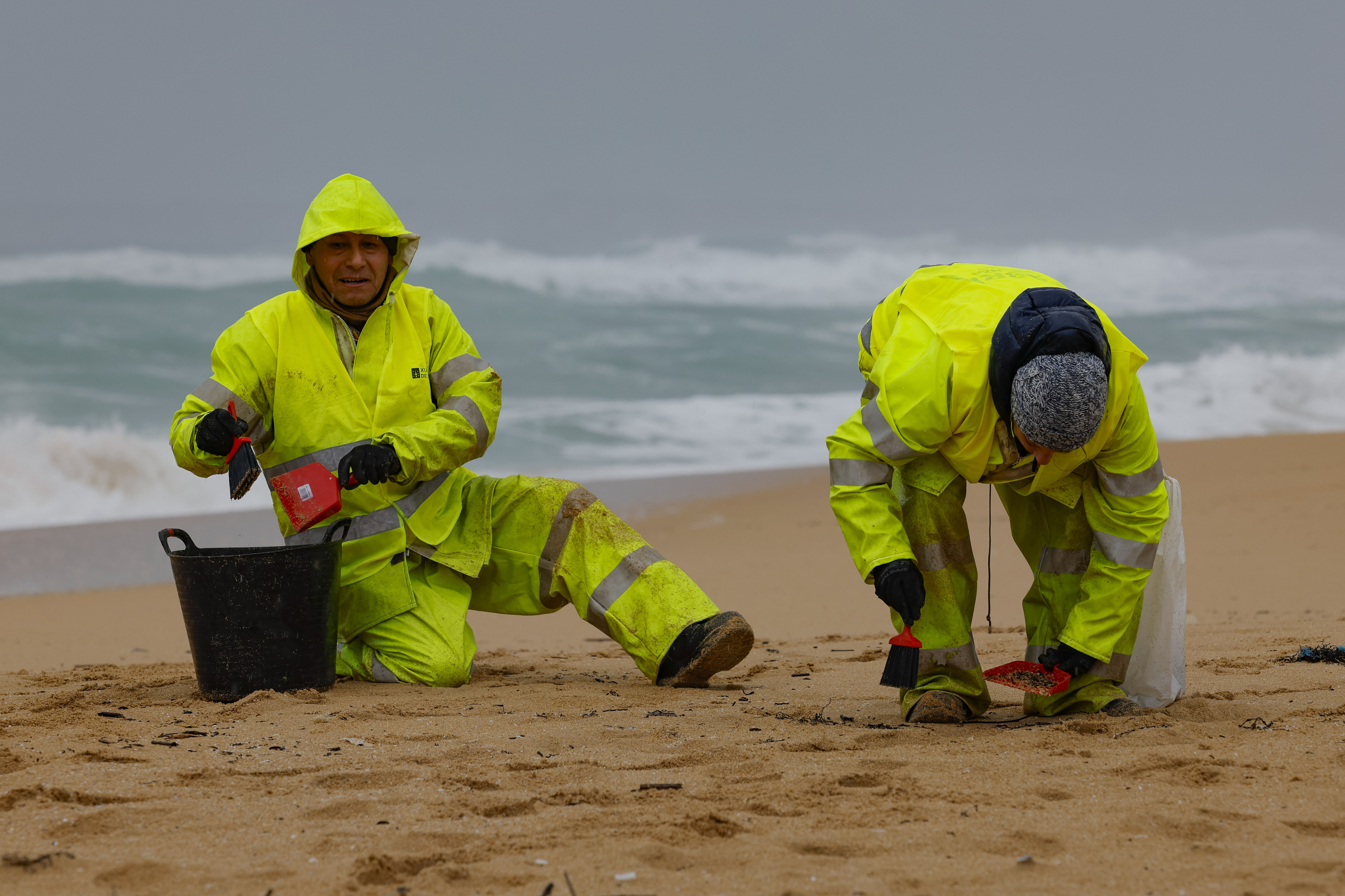 Operarios de empresas contratadas por la Xunta retiran los pellets de una playa gallega.