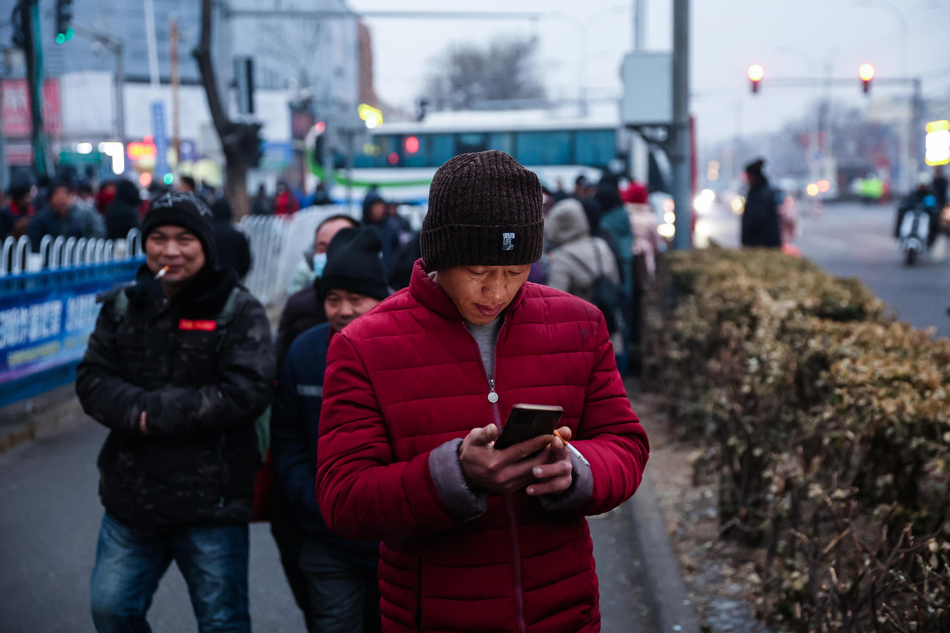 Un hombre usa su telfono mientras camina por una calle de  Pekn.