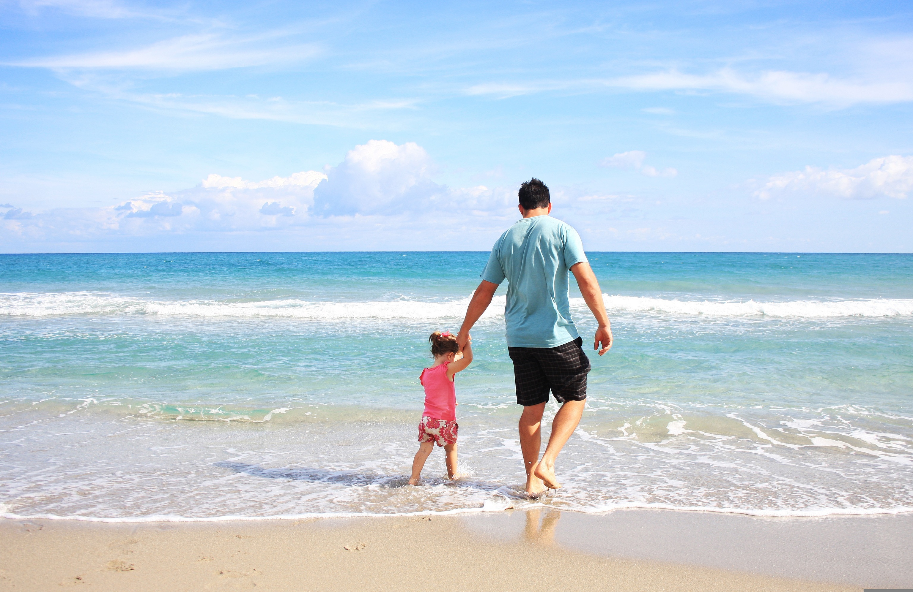 Un padre pasea con su hija por la playa.
