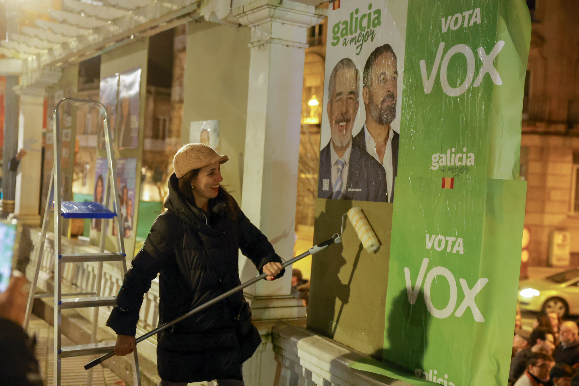 Una mujer coloca un pster de Vox durante la pegada de carteles electorales, en el inicio de campaa, en Orense.