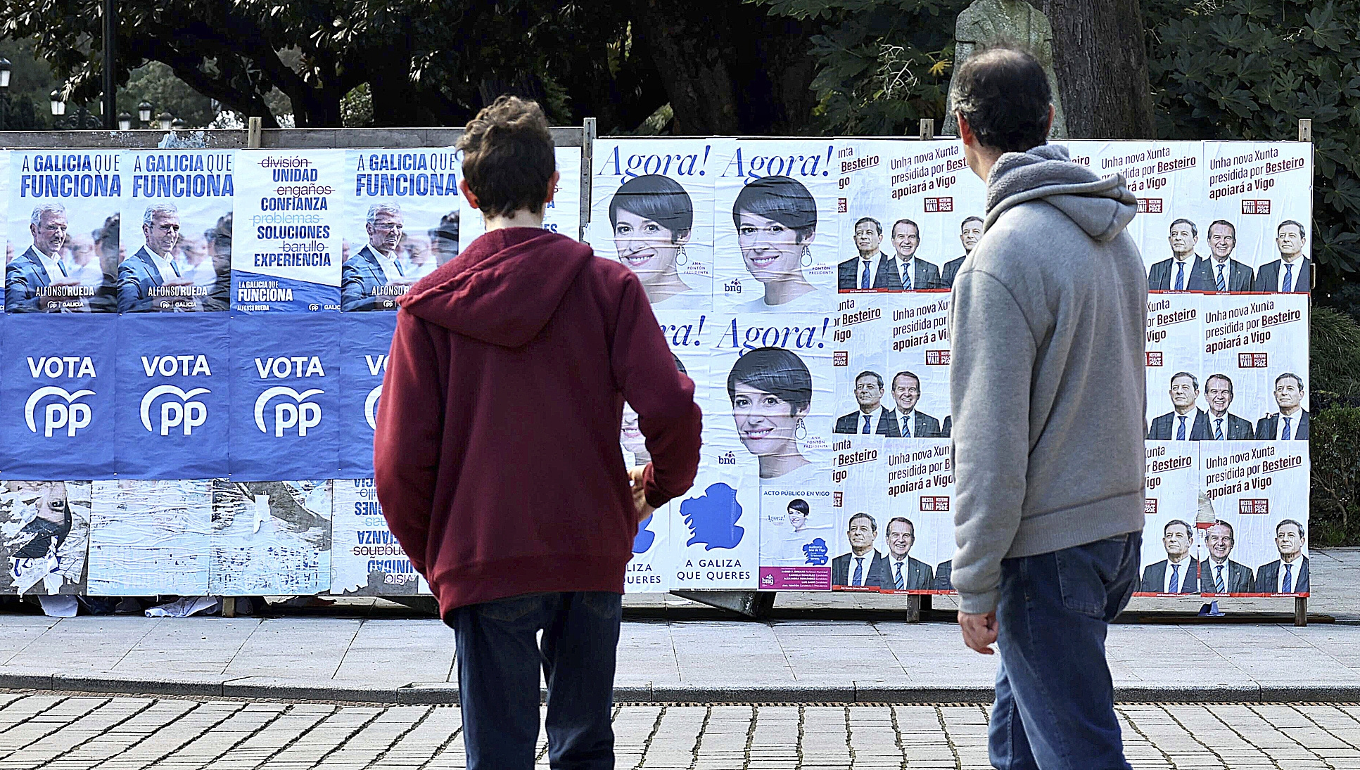 Dos personas observan ayer en una calle de Vigo un panel con los carteles electorales de PP, BNG y PSOE.