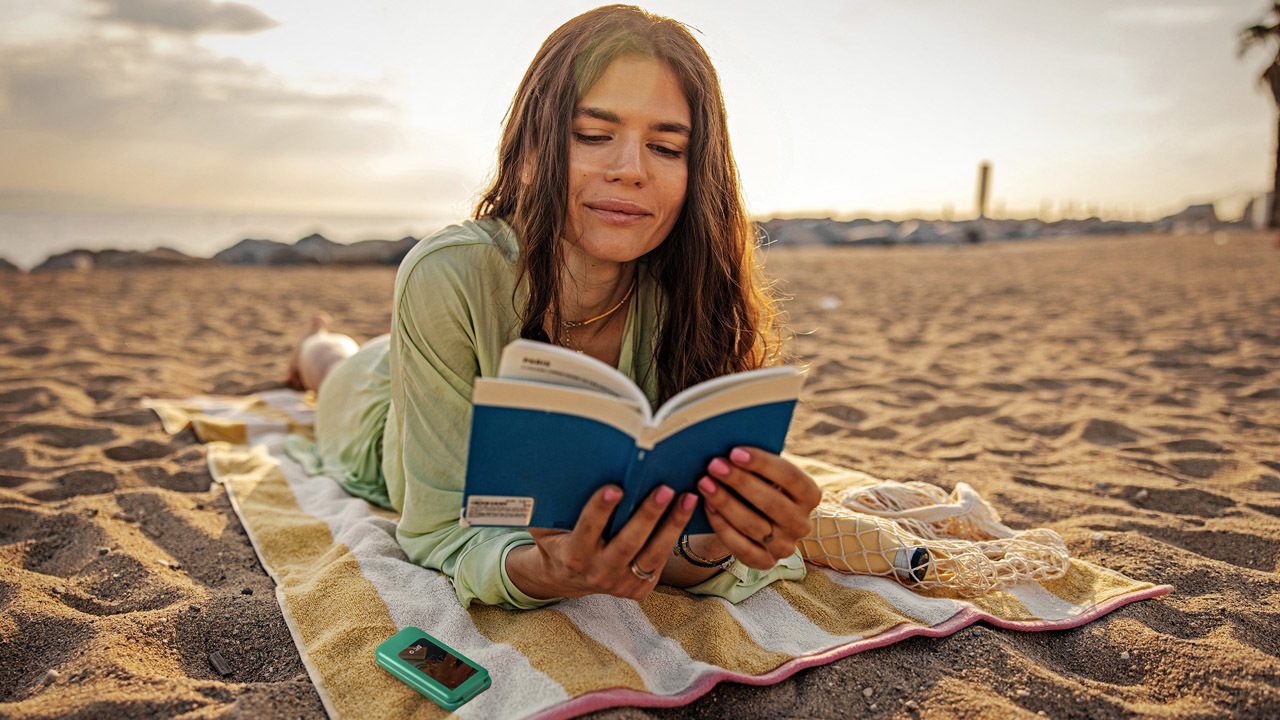 A girl holding a phone and reading a paper book