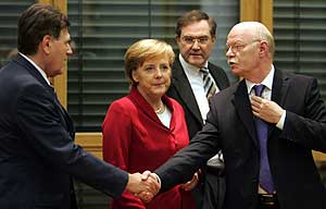 El ex ministro de Defensa (dcha.) saluda al nuevo titular de Economía, en presencia de la futura canciller, Merkel. (Foto: REUTERS)