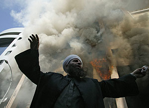 Un clrigo habla a los congregados junto al consulado en llamas. (Foto: AFP)