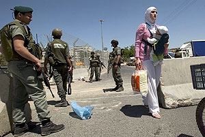 Una mujer palestina con su hijo en brazos pasa delante de los soldados israeles. (Foto: EFE)