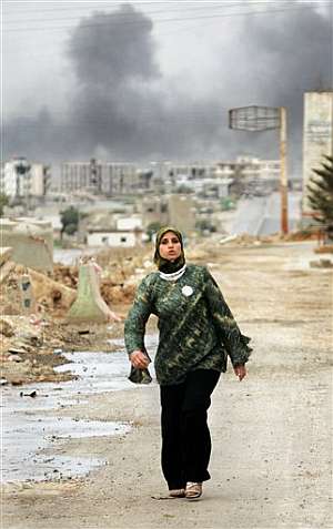 Una mujer camina mientras al fondo se ve una columna de humo fruto de los combates. (Foto: AP)