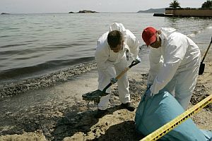 Dos operarios retiran fuel de la playa de Ses Figueretes. (Foto: EFE)