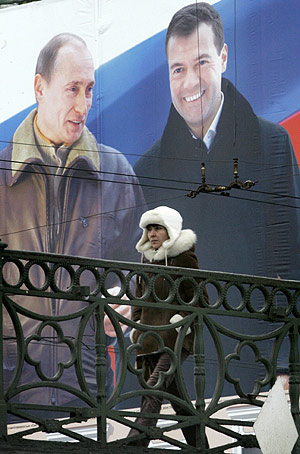 Una mujer camina por un puente bajo un cartel electoral con Putin y Medvédev. (Foto: AP)