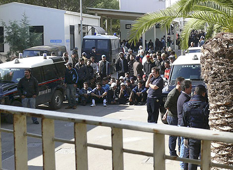 Los inmigrantes, sentados en el suelo ante las autoridades. | AP