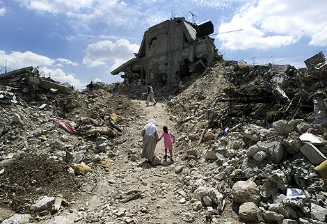 Una mujer y una nia caminan hacia una casa destrozada. | Reuters