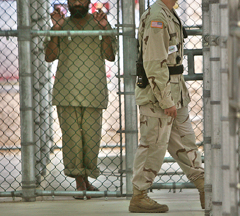Un guarda pasa delante de un preso en Guantnamo.| Afp