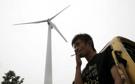 Un hombre fuma bajo un aerogenerador en Nantong, en la provincia china de Jiangsu. | AFP