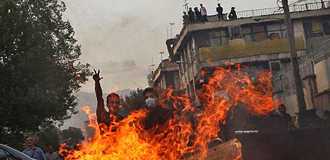 Un manifestante hace la señal de la victoria ante un contenedor en llamas. | AP
