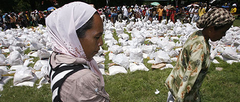 Dos mujeres recogen sacos de ayuda humanitaria en un campo de Mindanao. | Reuters