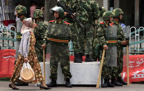 Una mujer Uigur pasa frente a unos policas paramilitares en Urumqi | Reuters