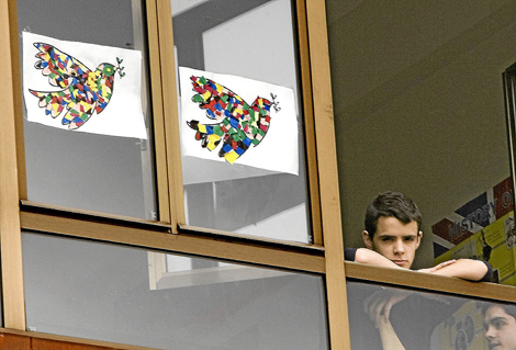 Un joven observa por la ventana de una escuela junto a dos murales que reclaman la paz. | C. G.