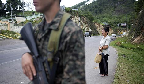 Una mujer espera el autobús junto a un control militar en las afueras de Tegucigalpa. | Reuters