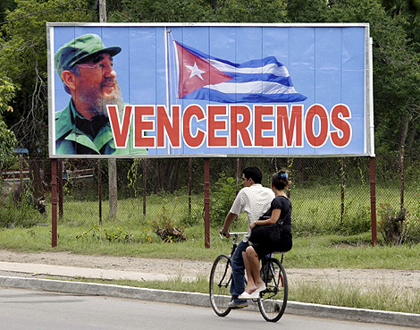Una pareja, en bicileta frente a uno de los crteles propagandsticos de la isla. | Reuters