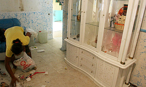 Una mujere recoge los restos del vandalismo de que ha sido objeto su vivienda. | Fernando Ruso