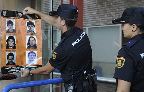 Dos miembros de la Polica Nacional retiran un cartel con los rostros de seis etarras ya detenidos. | Efe
