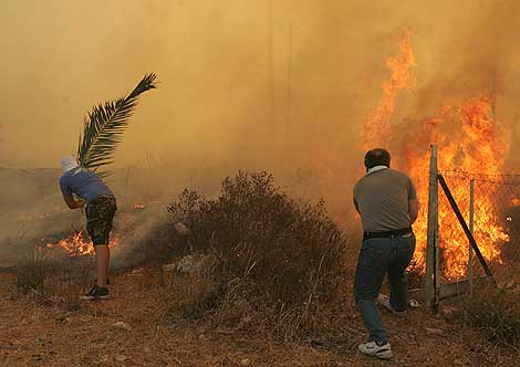 Dos ciudadanos griegos intentan apagar las llamas. | Efe