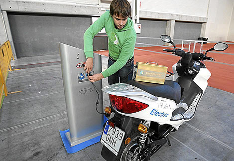 Un joven recarga una motocicleta ecolgica en un puesto elctrico. | J.M. Lostau