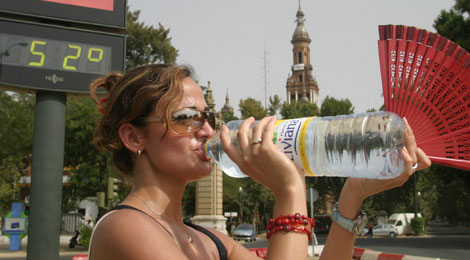 Una turista bebe agua ante un termómetro a 52 grados en verano. | Fernando Ruso