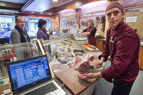 Mikel Izarzuaga corta unos filetes en su carnicería, con el ordenador sobre el mostrador. | Mitxi