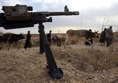 Varios afganos caminan frente al fusil de un soldado de la OTAN. | Reuters