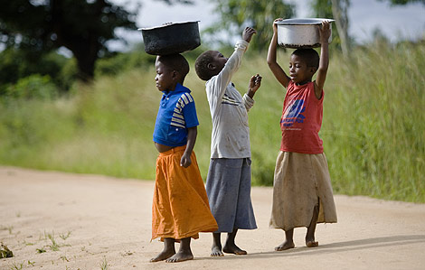 Tres nios llevan agua sobre sus cabezas, en Malawi. | Plan