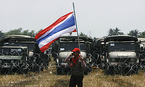 Un opositor sostiene la bandera tailandesa ante una barricada de coches policiales. | Reuters