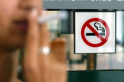 Una mujer con un cigarro delante de una seal de prohibido fumar. | ELMUNDO.es