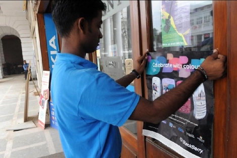 Un joven coloca un cartel de BlackBerry en una tienda india. | Afp