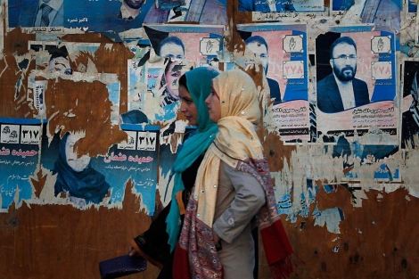 Dos mujeres afganas, ante los restos de carteles electorales. | AP