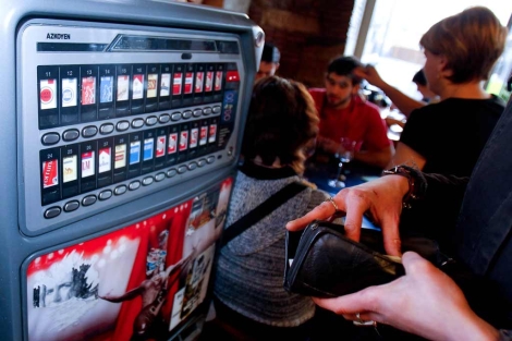 Una cliente compra tabaco en la mquina expendedora de un bar. | Justy