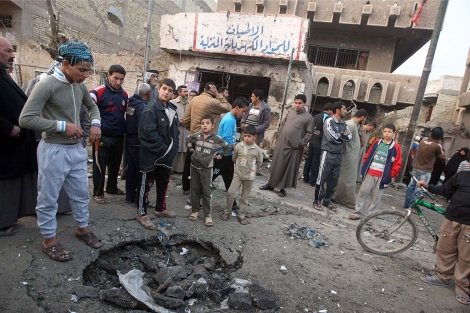 Un grupo de iraquíes observa el cráter que este jueves dejó un coche bomba en Bagdad. | AFP